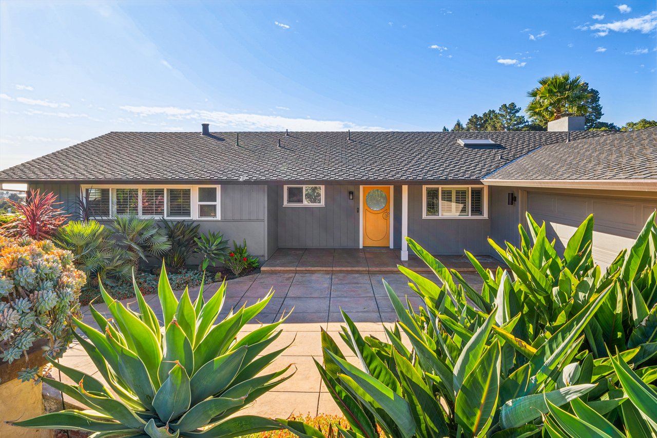 Single-level gray home with an orange entry door, tiled path, and drought-tolerant landscaping.
