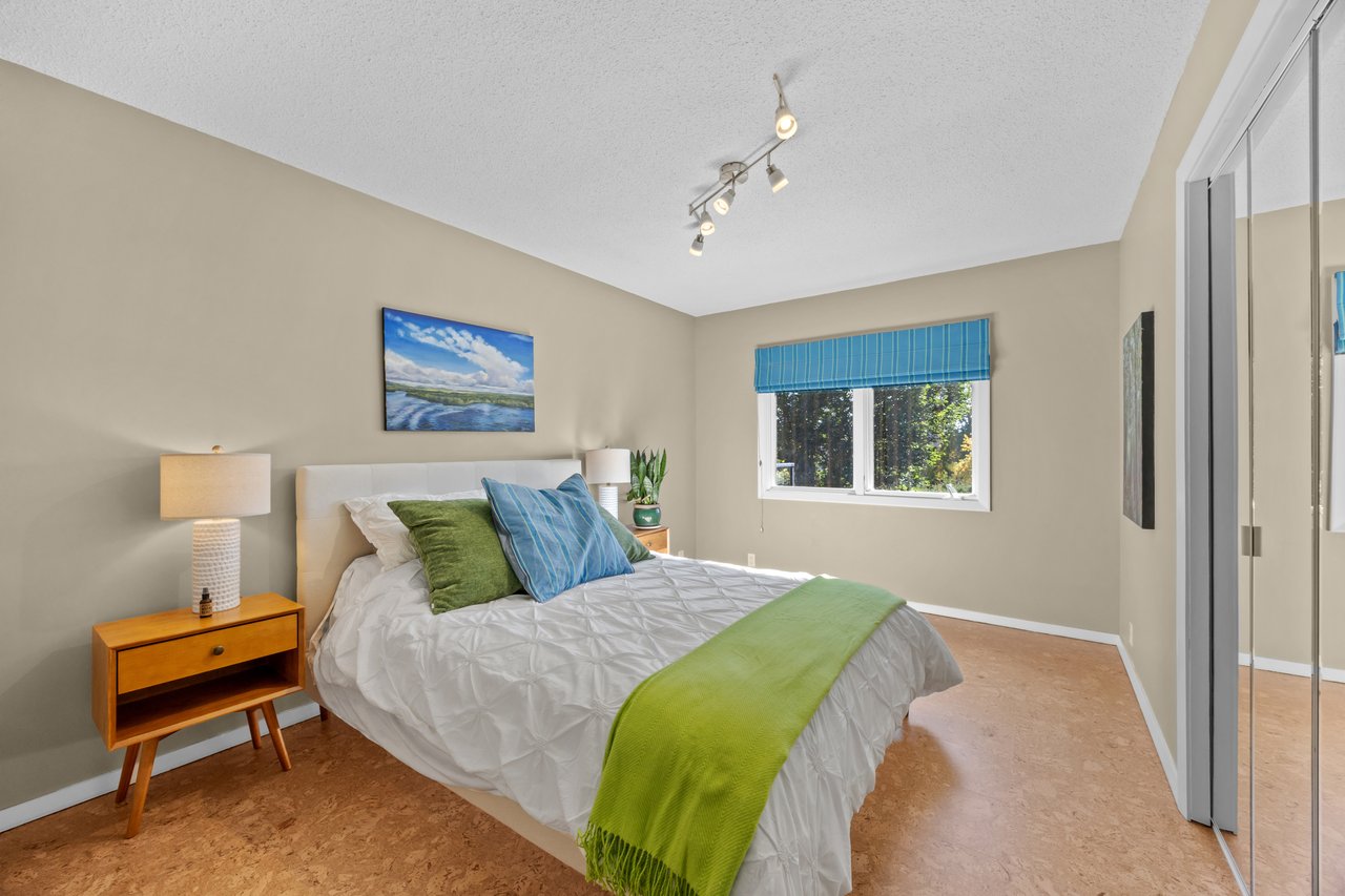 Bedroom with a white bed, green throw, blue window shade, and mirrored closet doors.