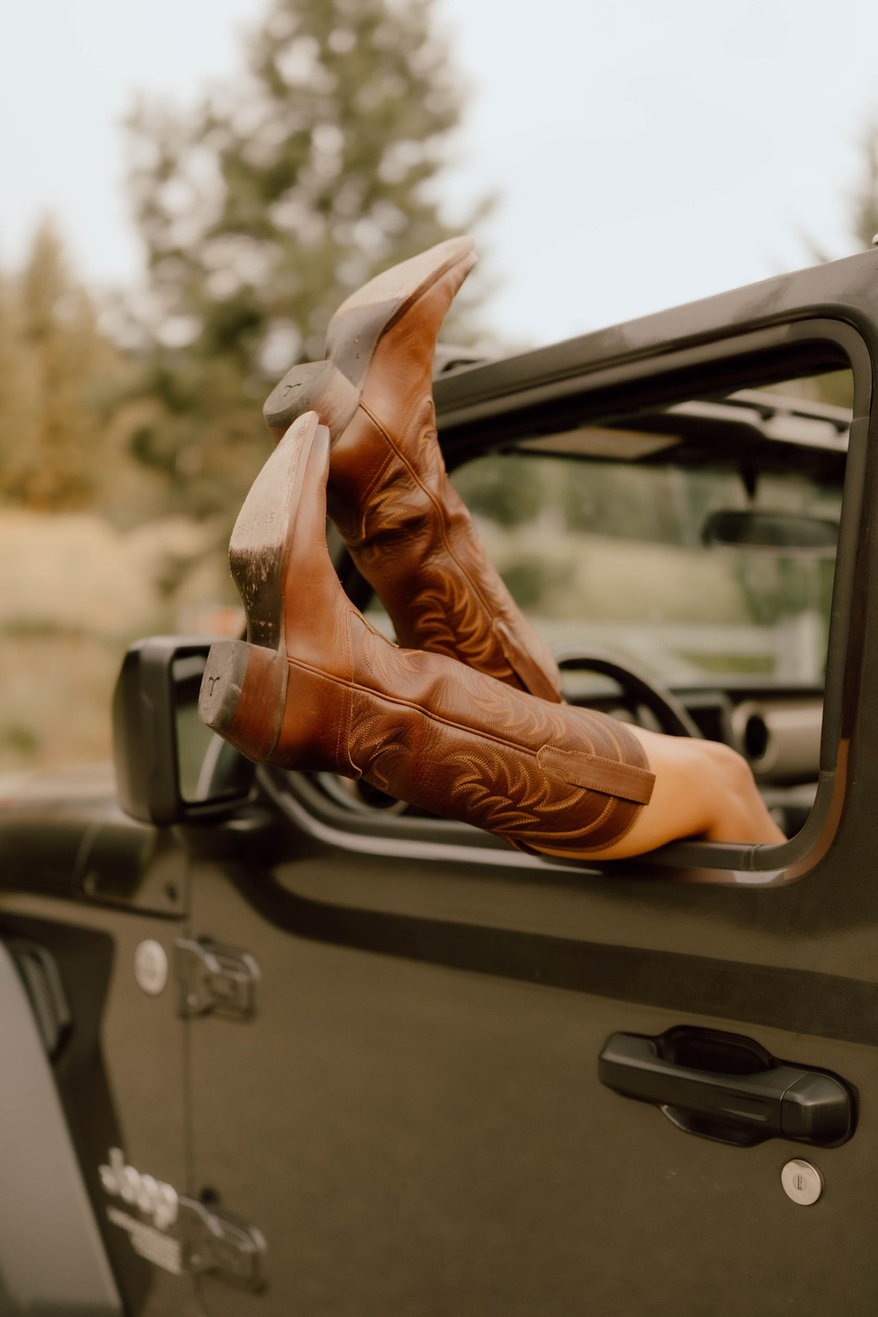 Brown cowboy boots propped out of an olive off-road vehicle’s open window.