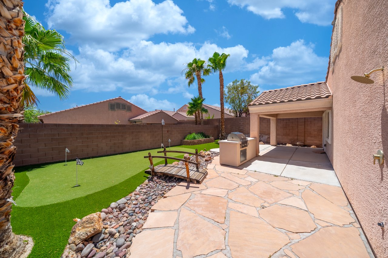 Backyard patio with a built-in grill, artificial-turf putting green, and palm trees.