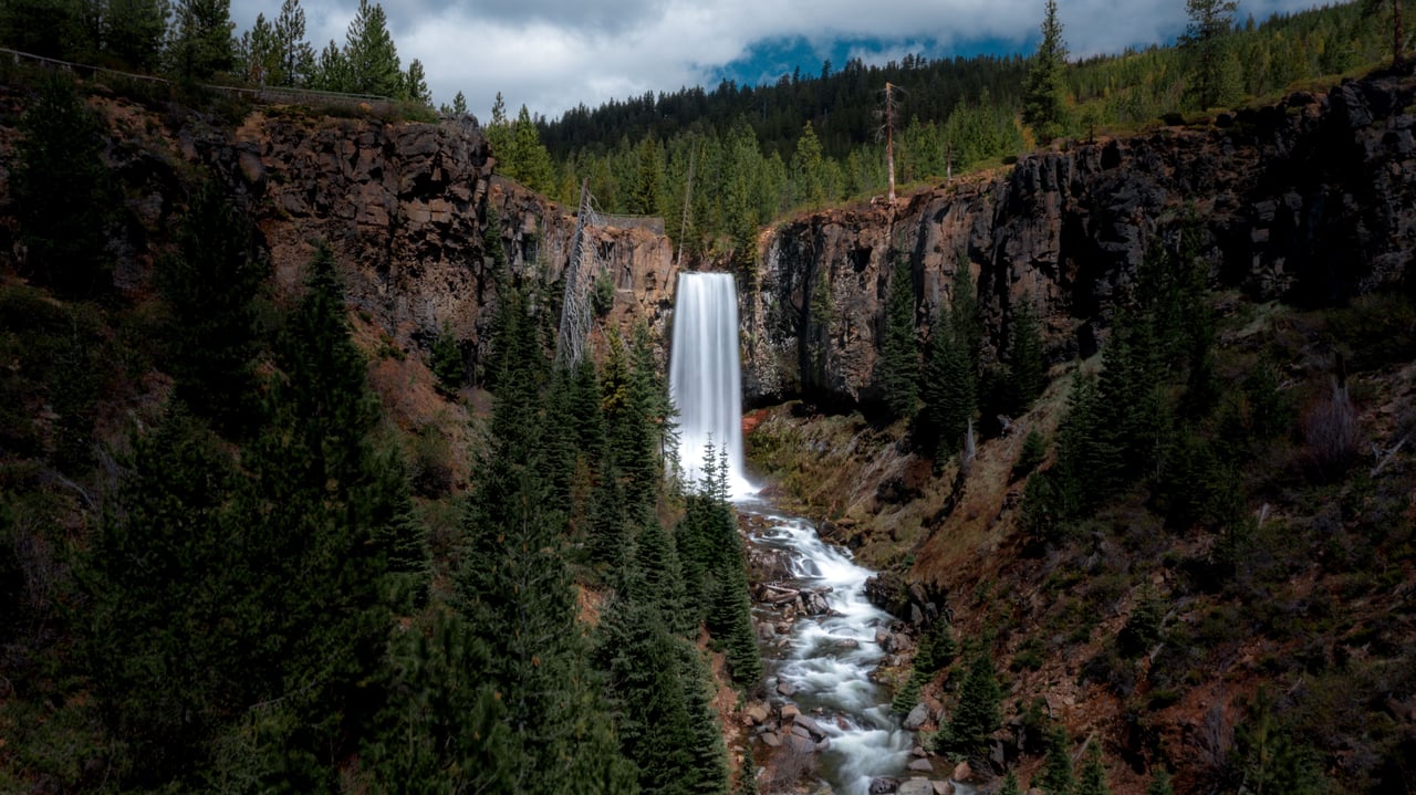 Waterfall flowing through a rocky gorge surrounded by evergreen forest.