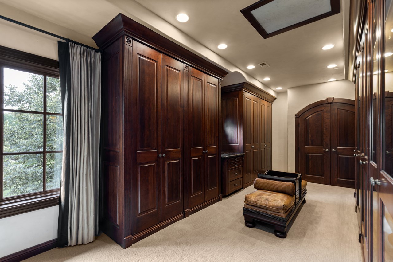Walk-in dressing room with dark wood wardrobes, arched double doors, and a leather-topped bench.