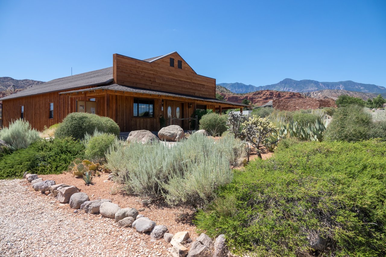 Wood-sided building amid desert landscaping, with red rock formations and mountains behind it.