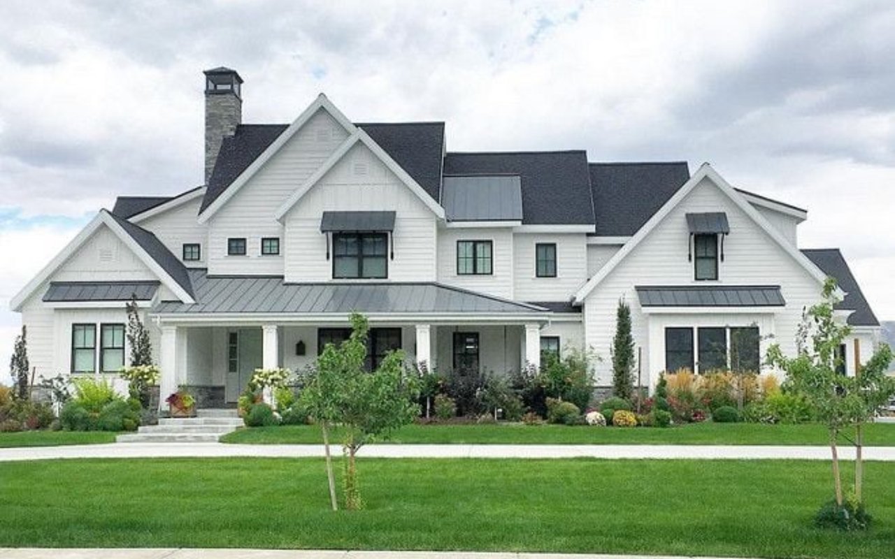 Large white two-story house with multiple gables, a covered porch, and landscaped gardens.