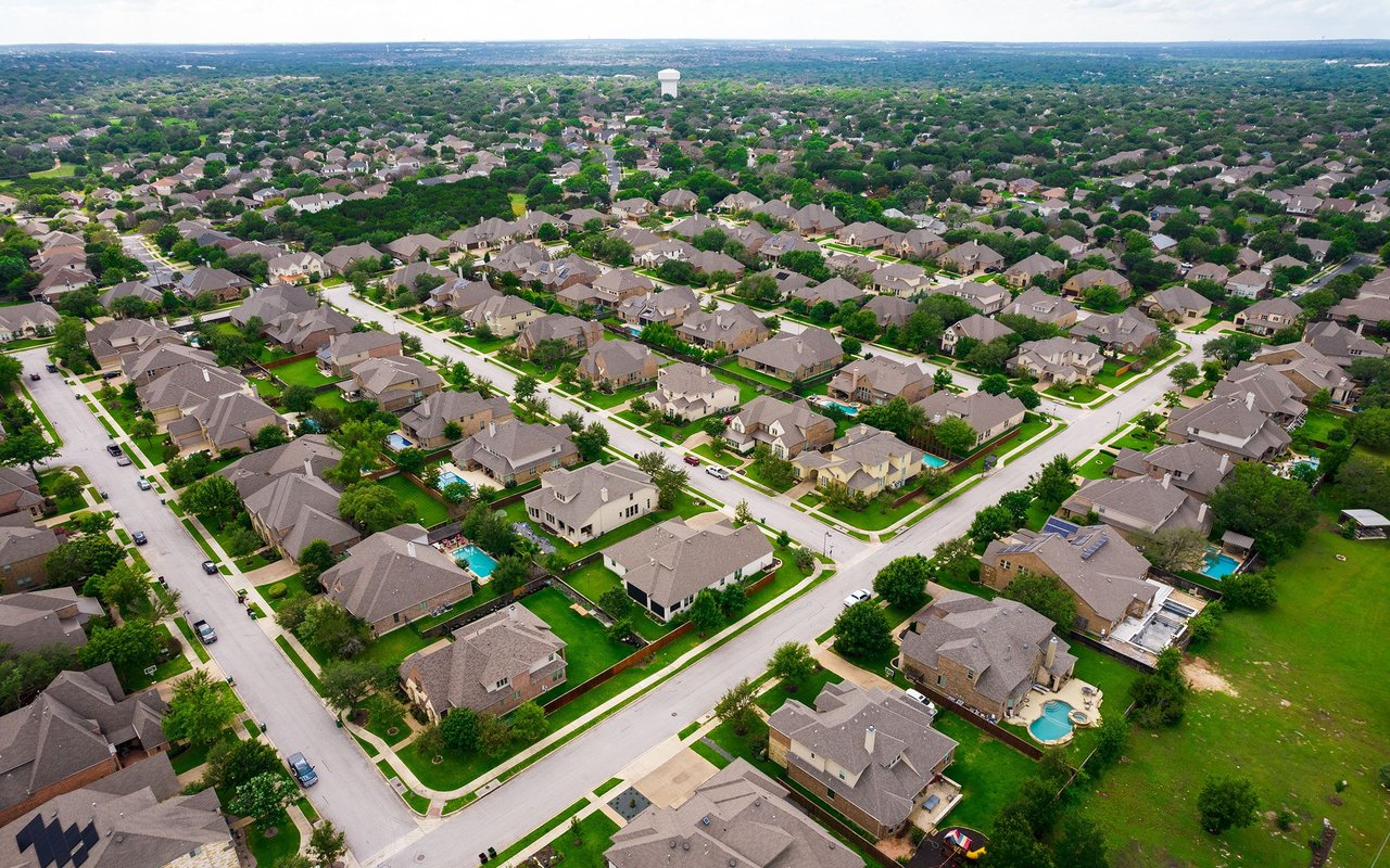 Aerial view of a leafy suburban neighborhood with detached homes, backyard pools, and a distant water tower.