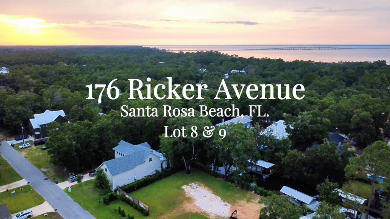 Aerial view of a wooded waterfront neighborhood and vacant lot at sunset.