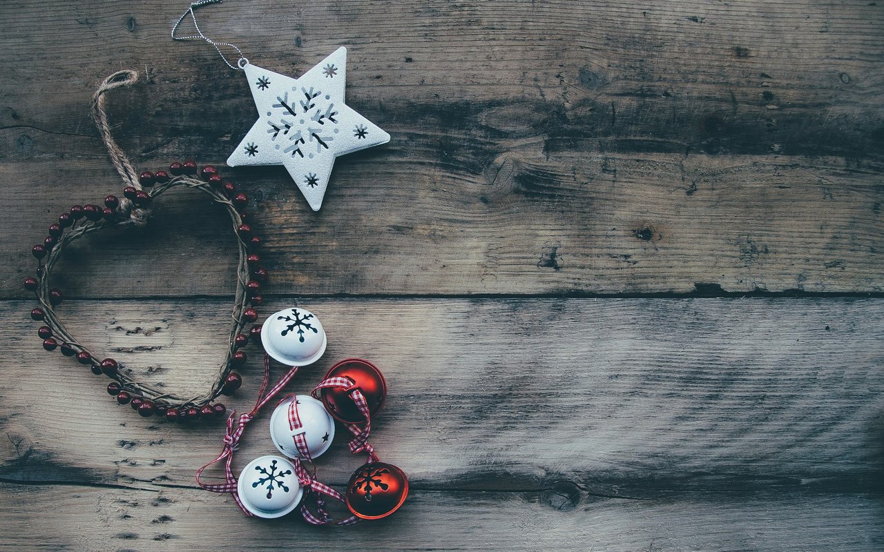 A top-down view of Christmas decorations, including a heart-shaped wreath, bells, and a star, on a rustic wood surface.