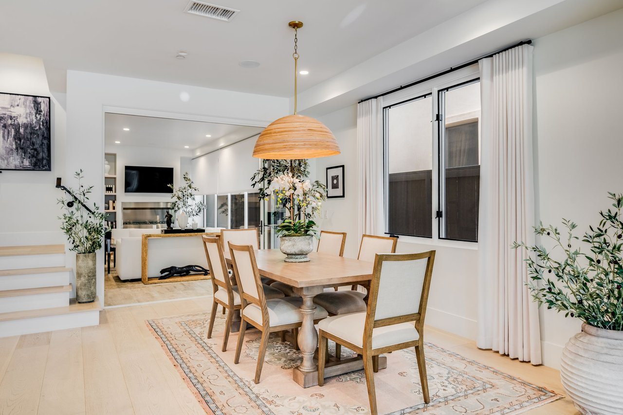 Dining area with a light wood table, upholstered chairs, woven pendant, and adjoining living room.