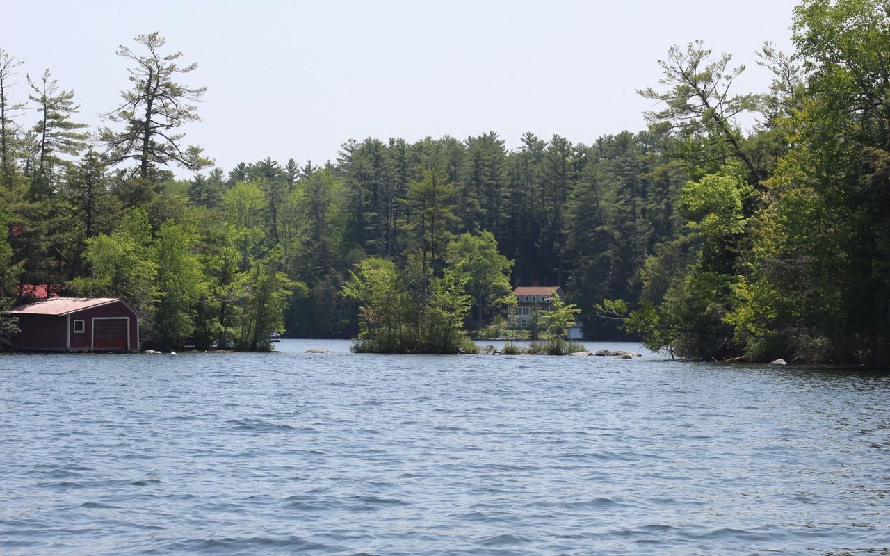 Wooded lake with a red boathouse on the shore and a house across the water.