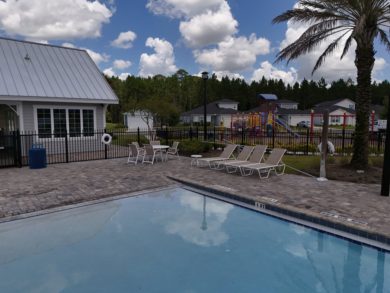 Community pool with lounge chairs and a fenced playground in the background.