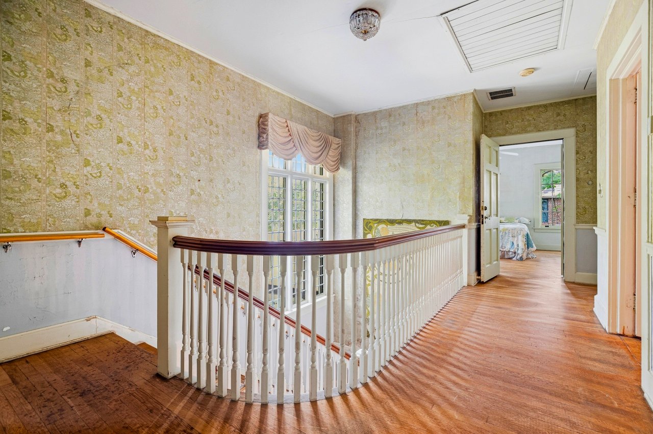 Upstairs landing with a curved white balustrade, patterned wallpaper, and polished hardwood floors.