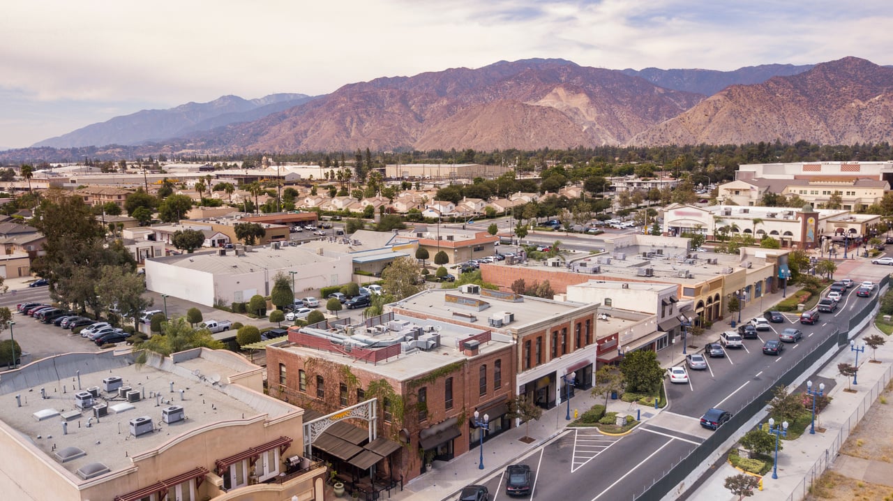 Aerial view of downtown Azusa, with low-rise shops and streets beneath rugged mountains.