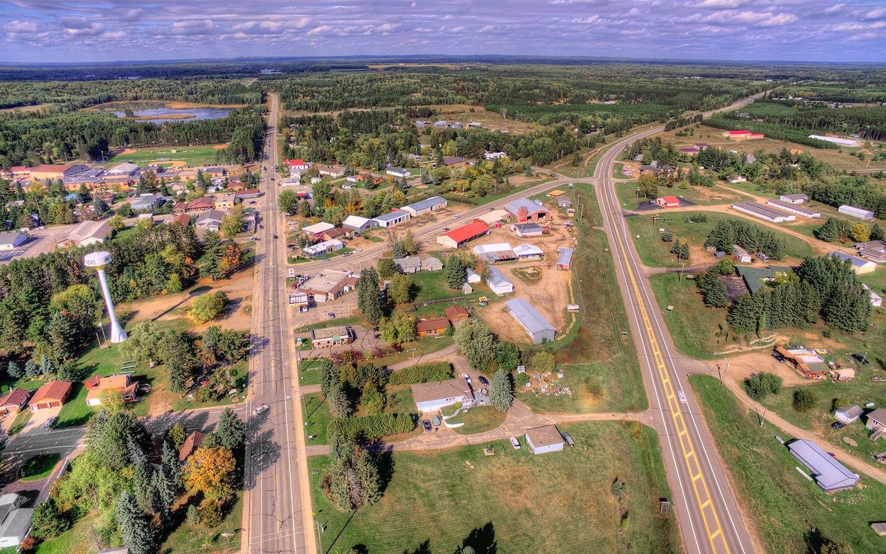 Aerial view of a small town with a water tower, scattered buildings, and wooded countryside.