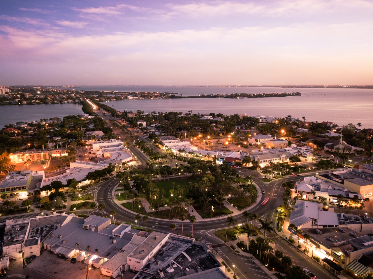 Aerial view of downtown Sarasota at dusk, with Sarasota Bay and illuminated streets.
