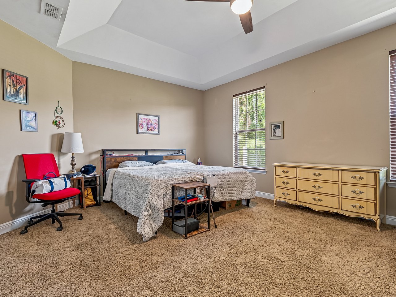 Bedroom with a tray ceiling, a bed, yellow dresser and red chair.