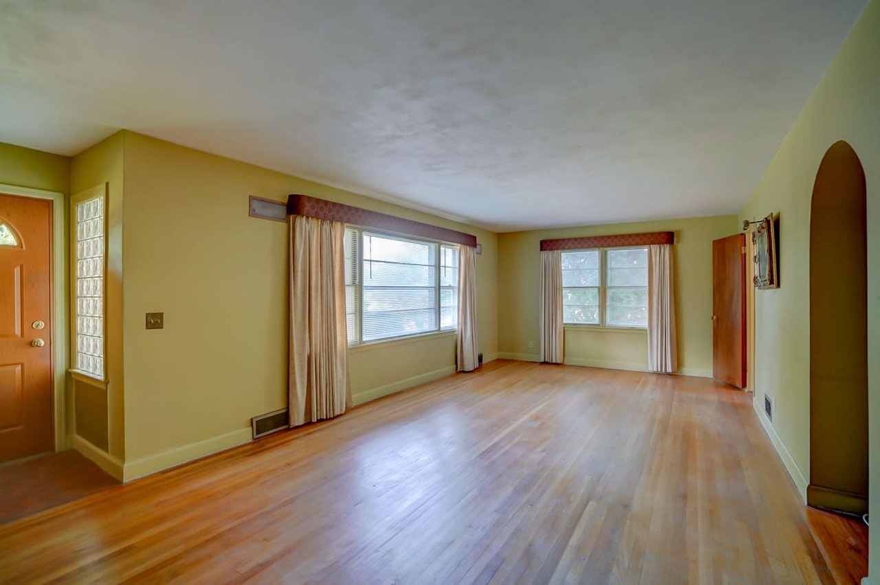 Unfurnished living room with hardwood floors, two curtained windows, and an arched doorway.