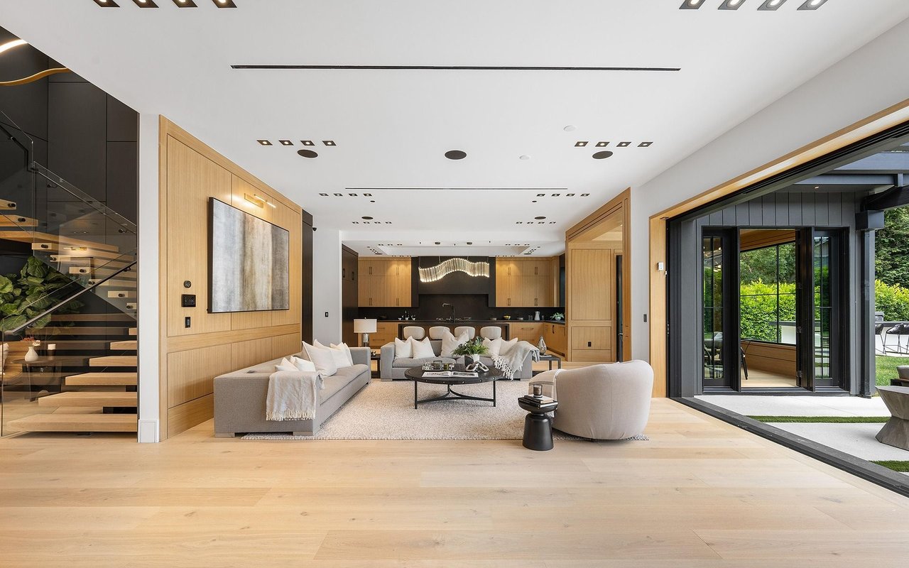 Open-plan living room with pale wood paneling, a floating staircase, and garden-facing glass doors.