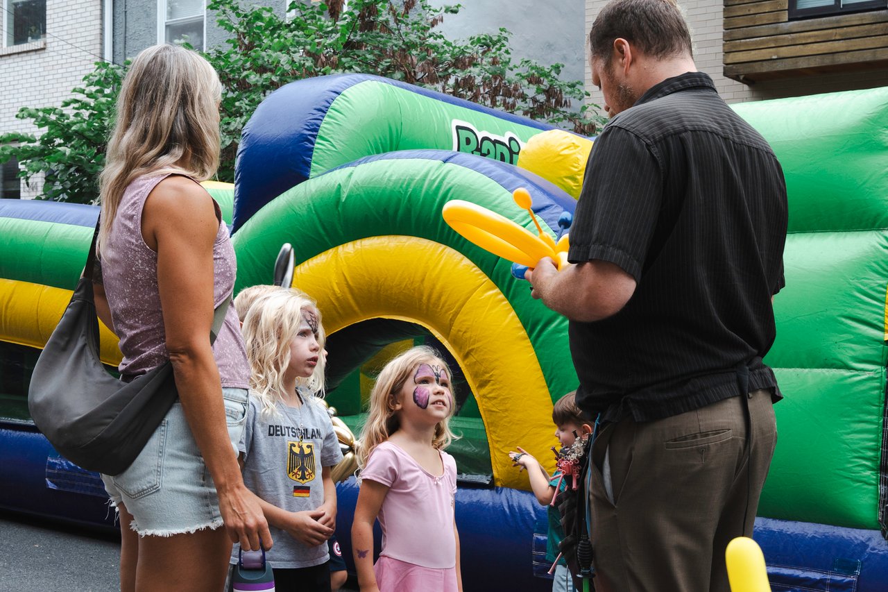 Children and adults gather beside a colorful bounce house at a neighborhood block party.
