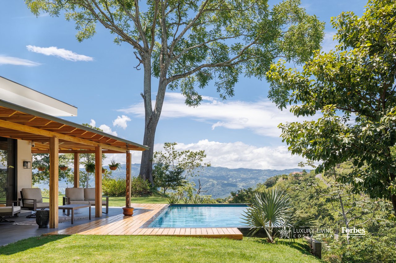 Modern home with a timber patio and infinity pool overlooking a green mountain valley.