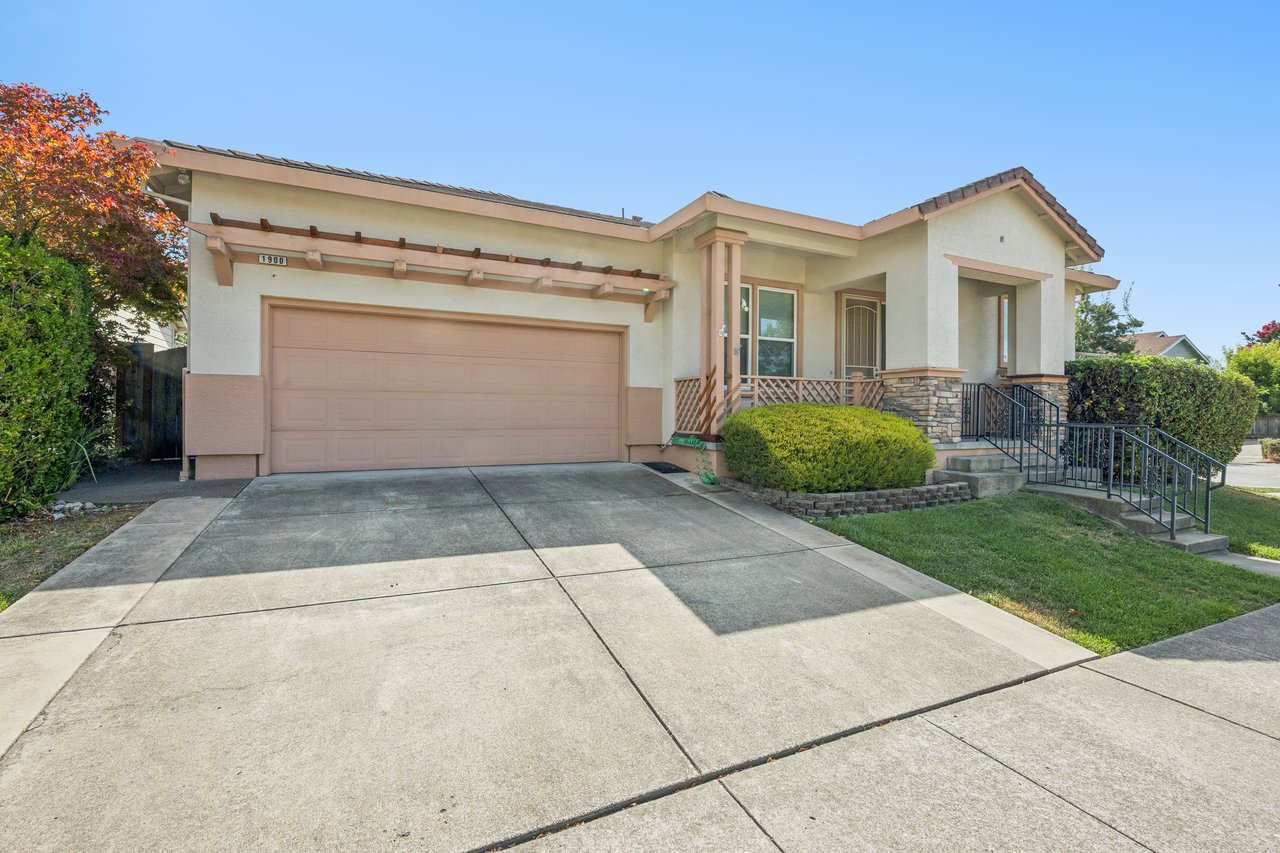 Single-story stucco home with a wide garage, stone accents, and a raised entrance with railings.