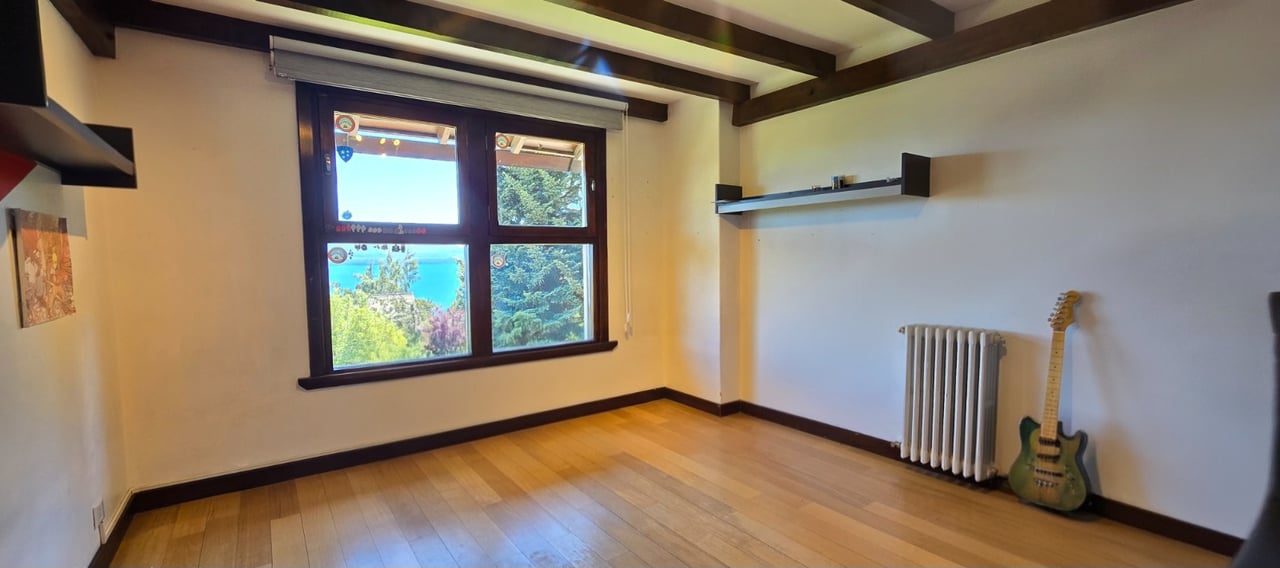 Unfurnished room with exposed ceiling beams, a guitar, and a window overlooking water and trees.