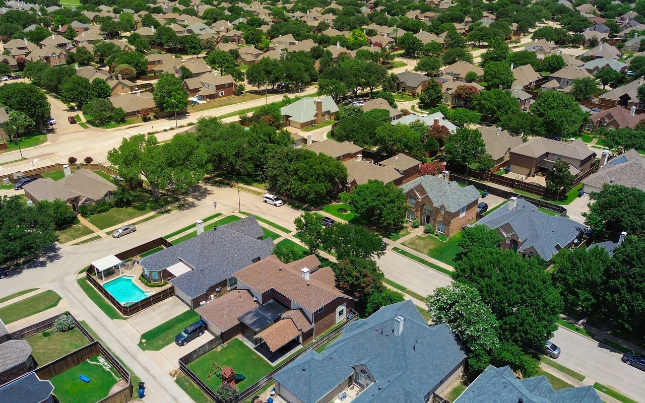 Aerial view of a tree-lined suburban neighborhood with detached homes and a backyard pool.