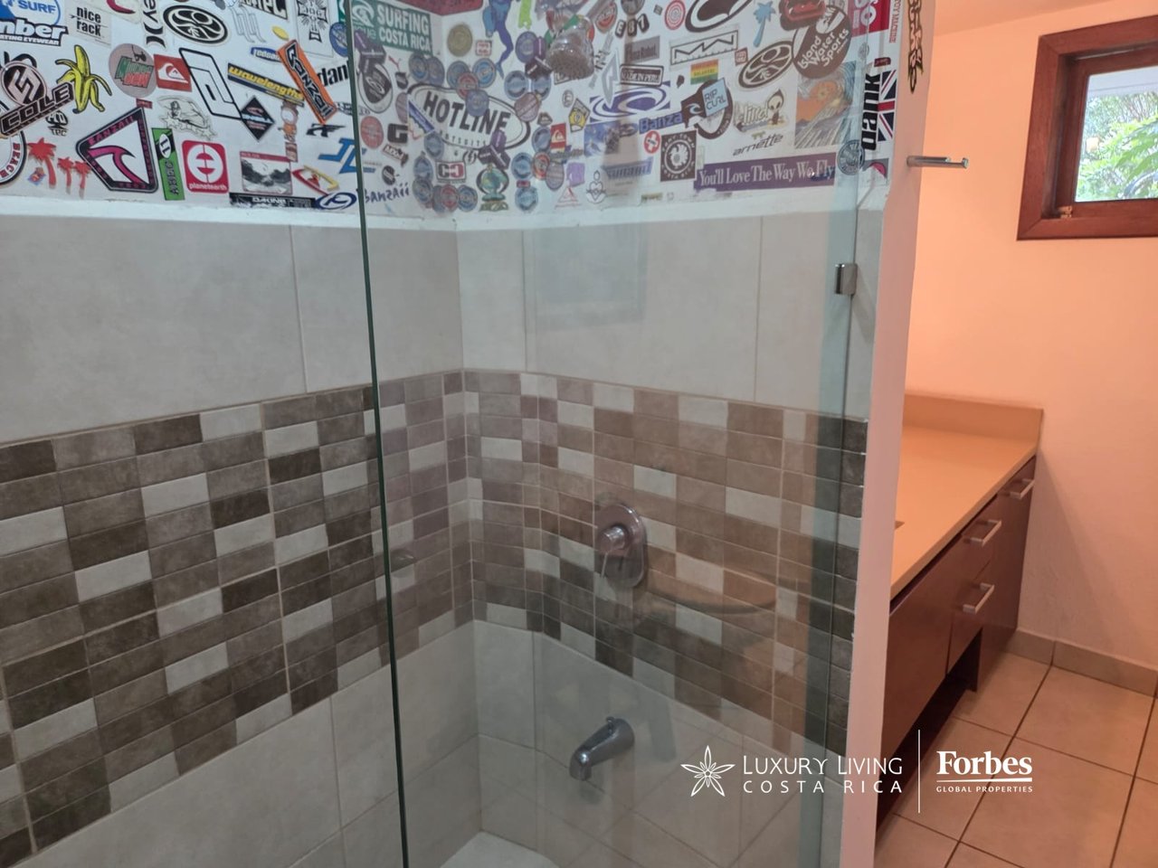 Bathroom shower with glass enclosure, checkerboard tile accents, and a wall covered in surf stickers.