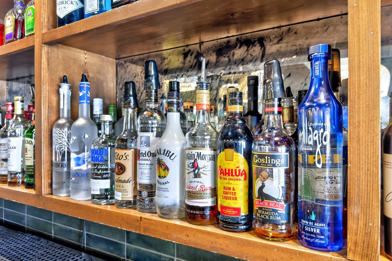 Restaurant bar lined with liquor bottles, including prominent blue Milagro and Goslings bottles.