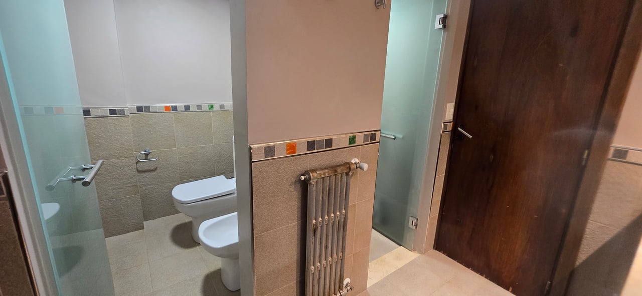 Bathroom with a glass shower enclosure, toilet and bidet, tiled walls, and a tall radiator.