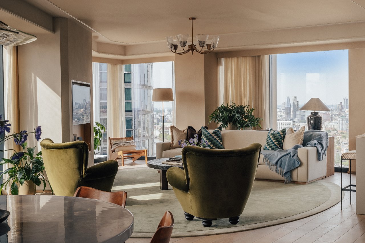 Living room with olive-green armchairs, cream sofa and floor-to-ceiling windows overlooking London.