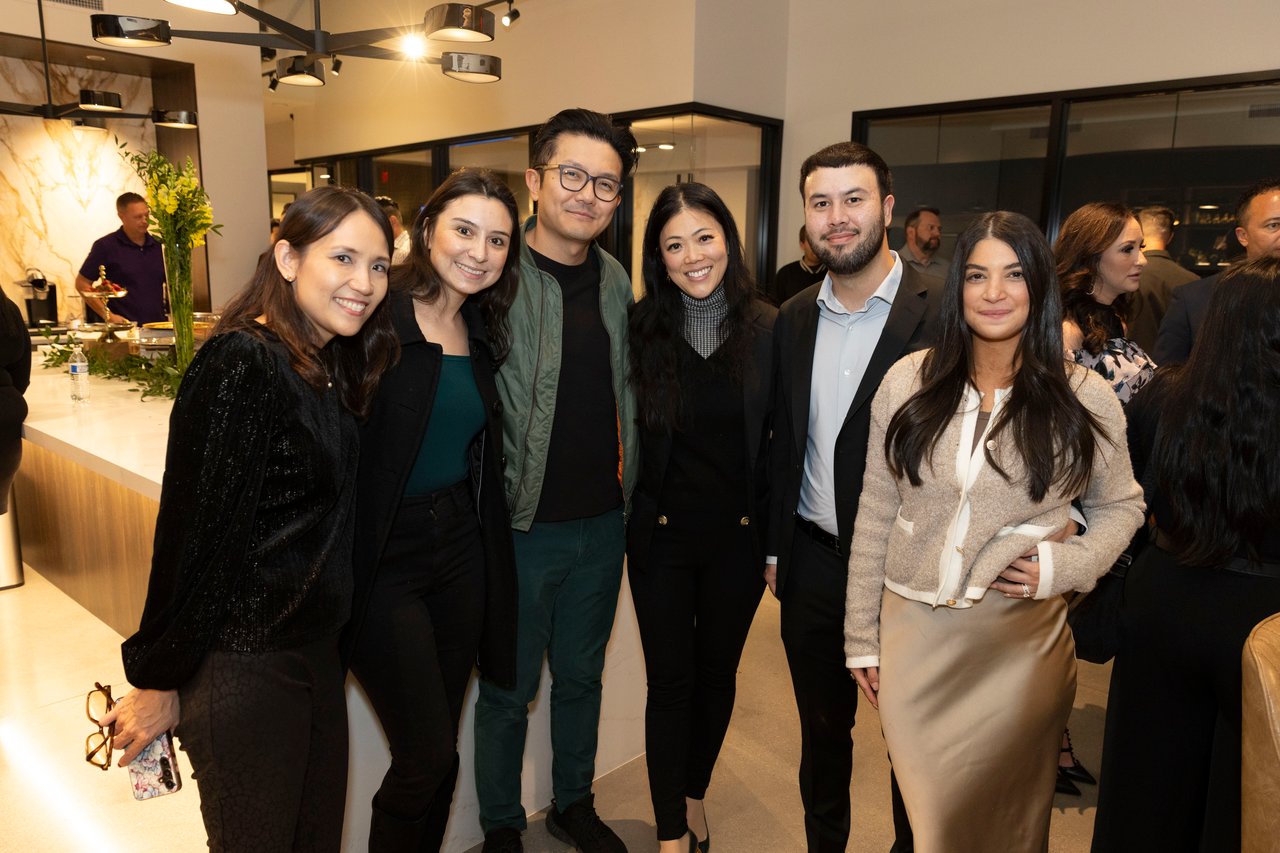 Six adults pose together at a client appreciation event inside a modern venue.