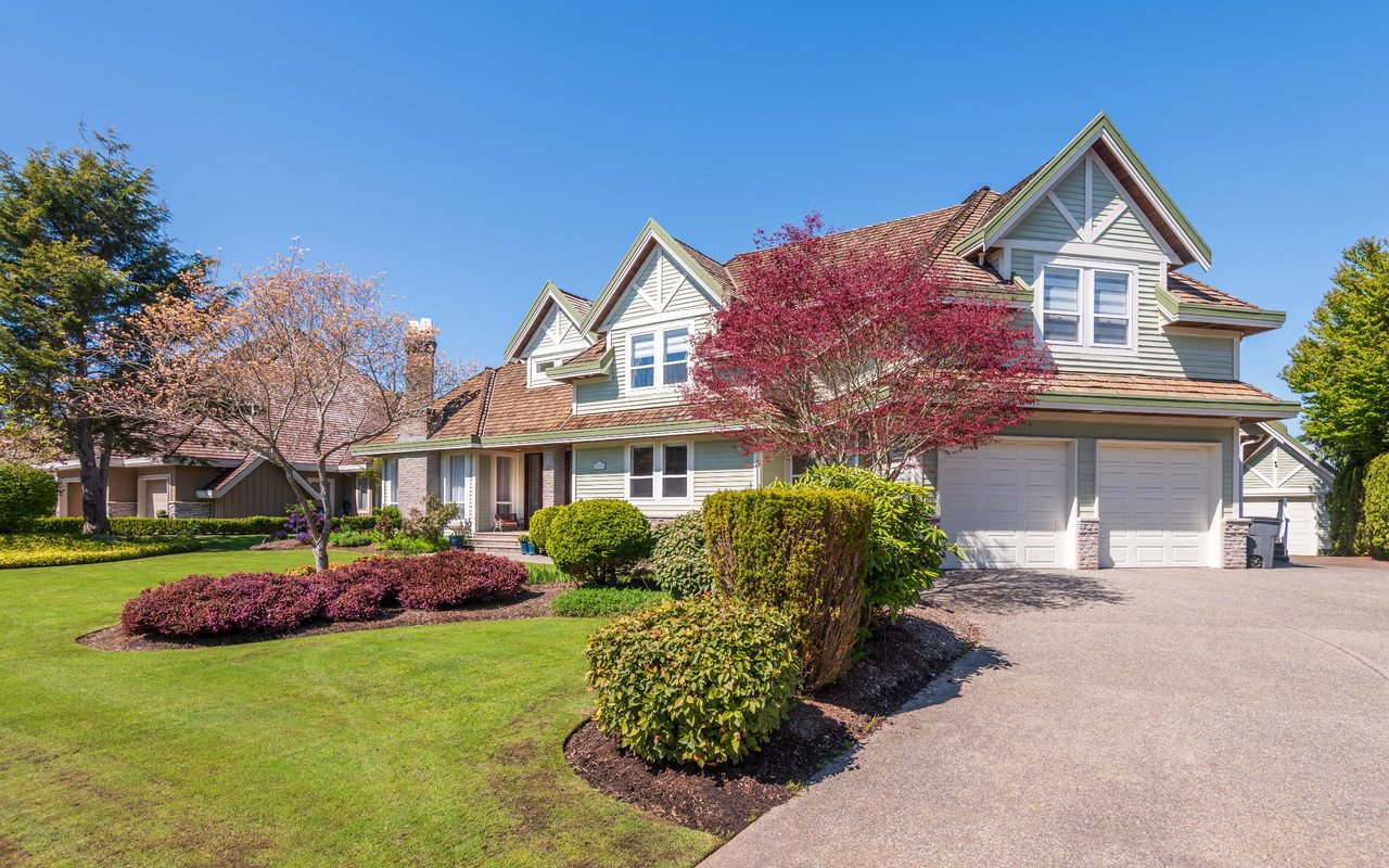 Two-story pale green home with multiple gables, a two-car garage, and landscaped front lawn.
