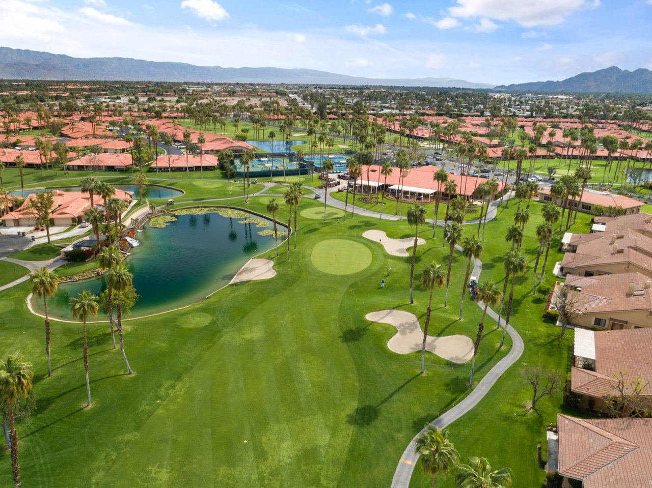 Aerial of Chaparral Country Club in Palm Desert: red tile roofs, a lake, palms, and the clubhouse beside a short golf hole, mountains on the horizon.