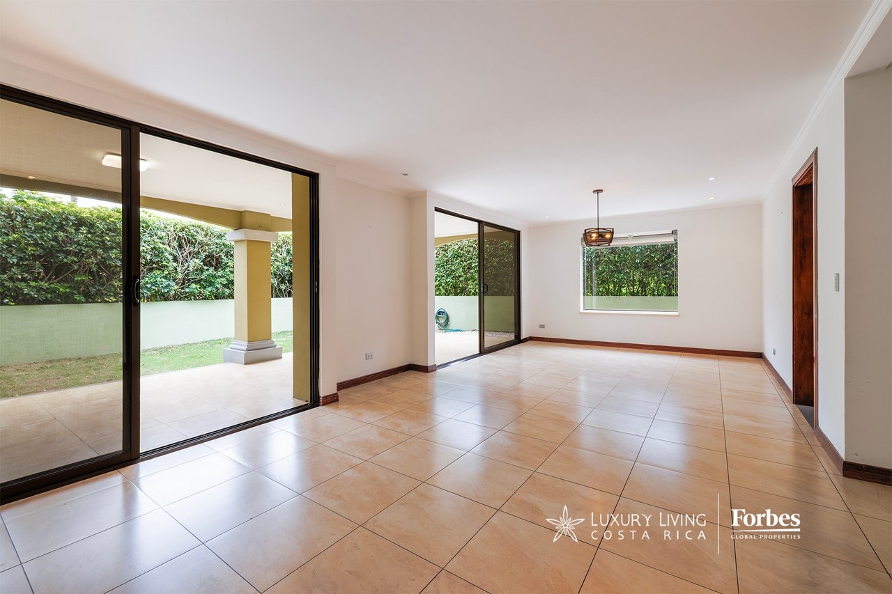 Empty tiled living room opening onto a garden terrace through sliding glass doors.