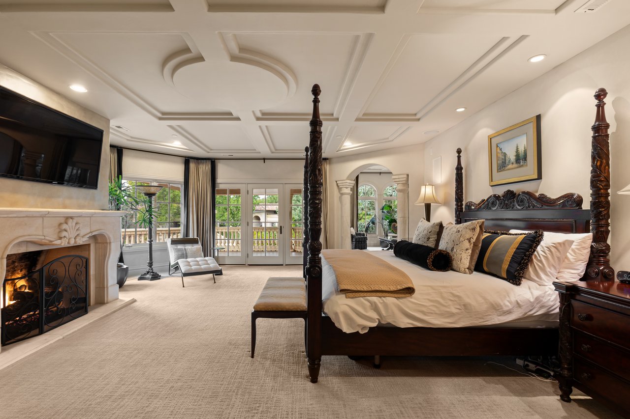 Bedroom with a carved four-poster bed, ornate fireplace, and French doors opening to a balcony.