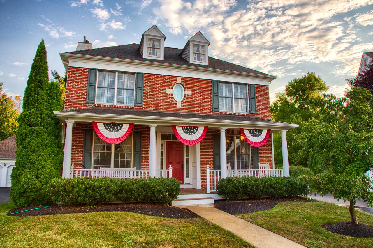 Red brick house with a columned porch, roof dormers, and patriotic bunting.