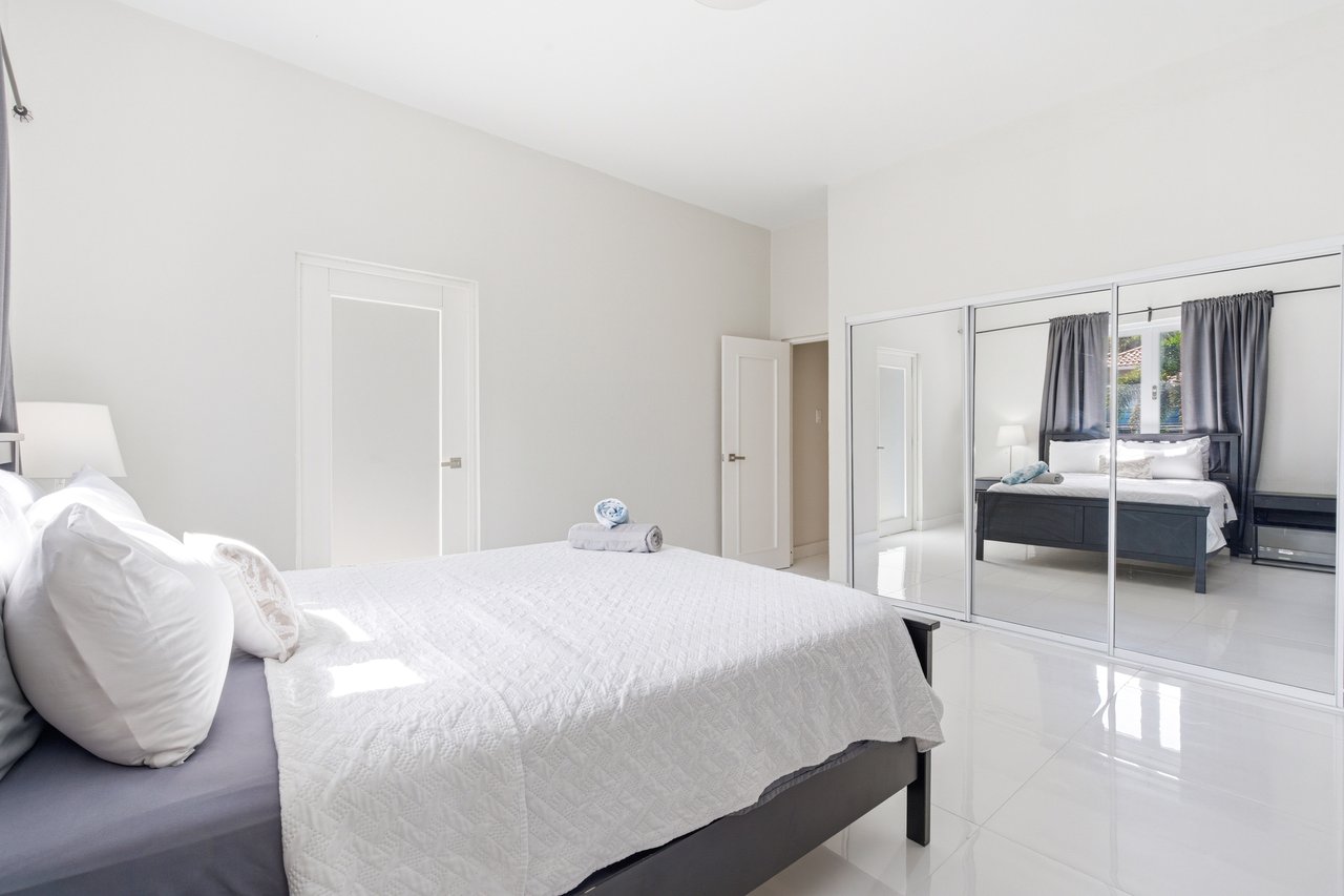 Bedroom with white quilted bedding, mirrored closet doors, and glossy tile floors.