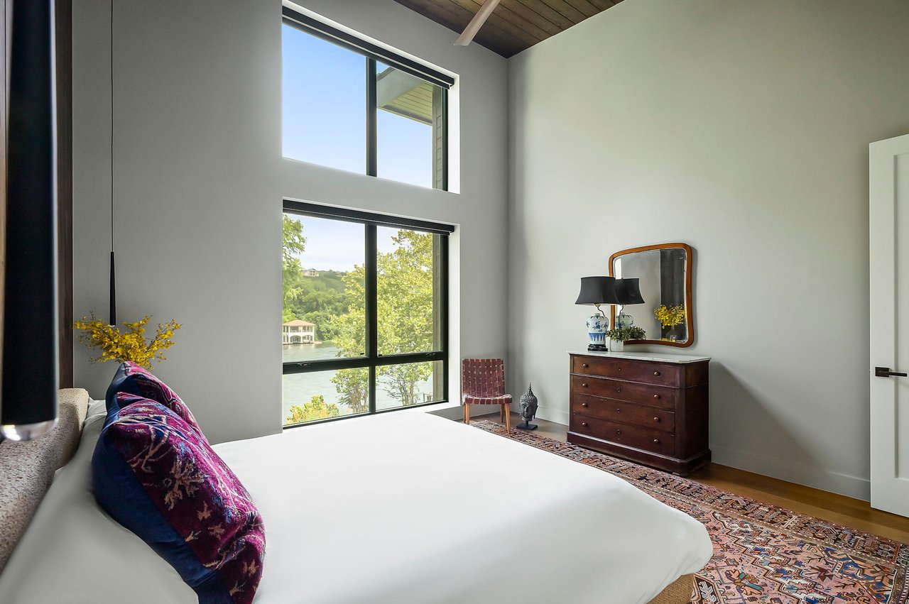 Primary bedroom with a vaulted ceiling and framed Lake Austin view, furnished by Liz MacPhail Interiors at 2403 Big Horn Drive, Austin.