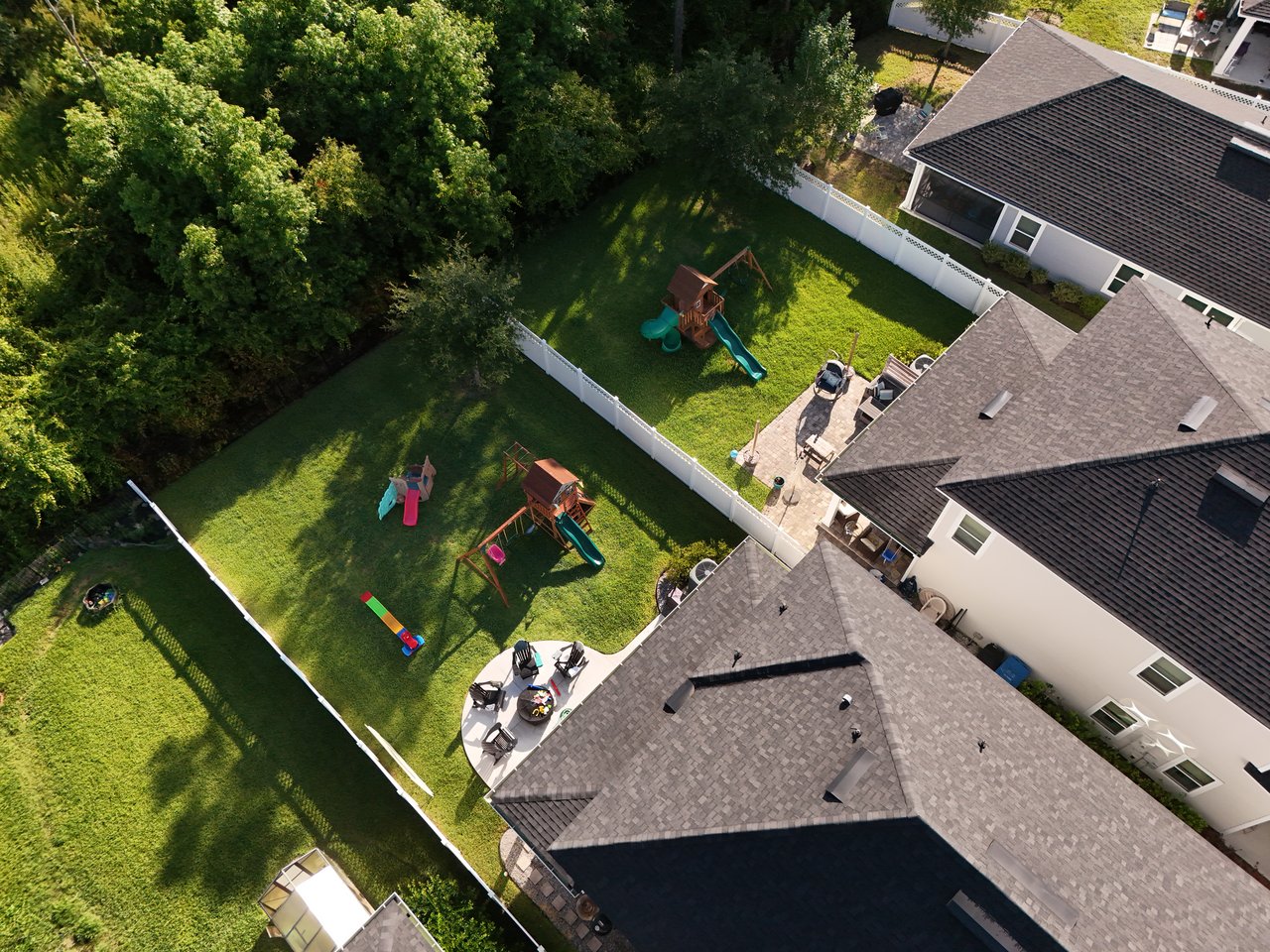 Aerial view of homes with fenced backyards, children's play structures, and dense trees.