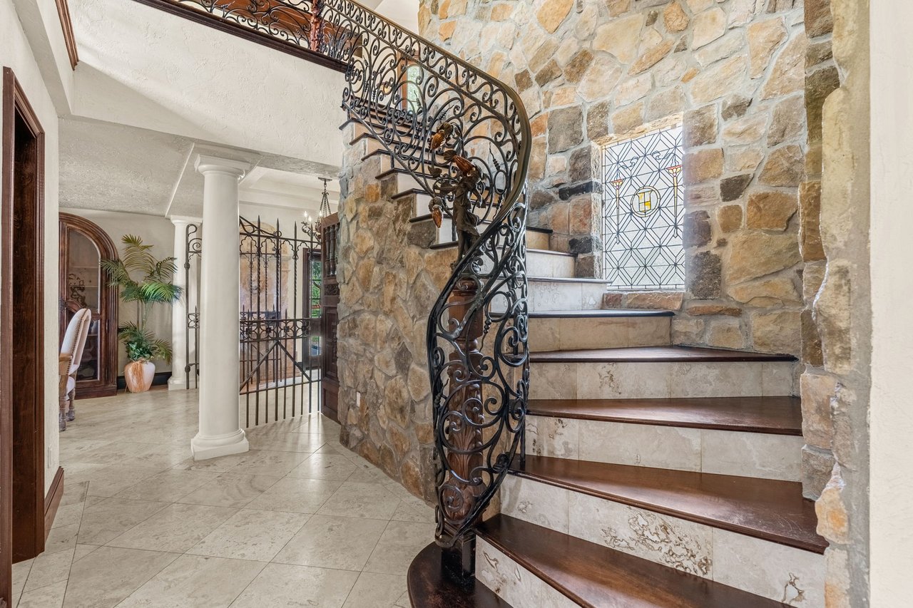 Grand foyer with a curved staircase, ornate iron railing, and stone walls.