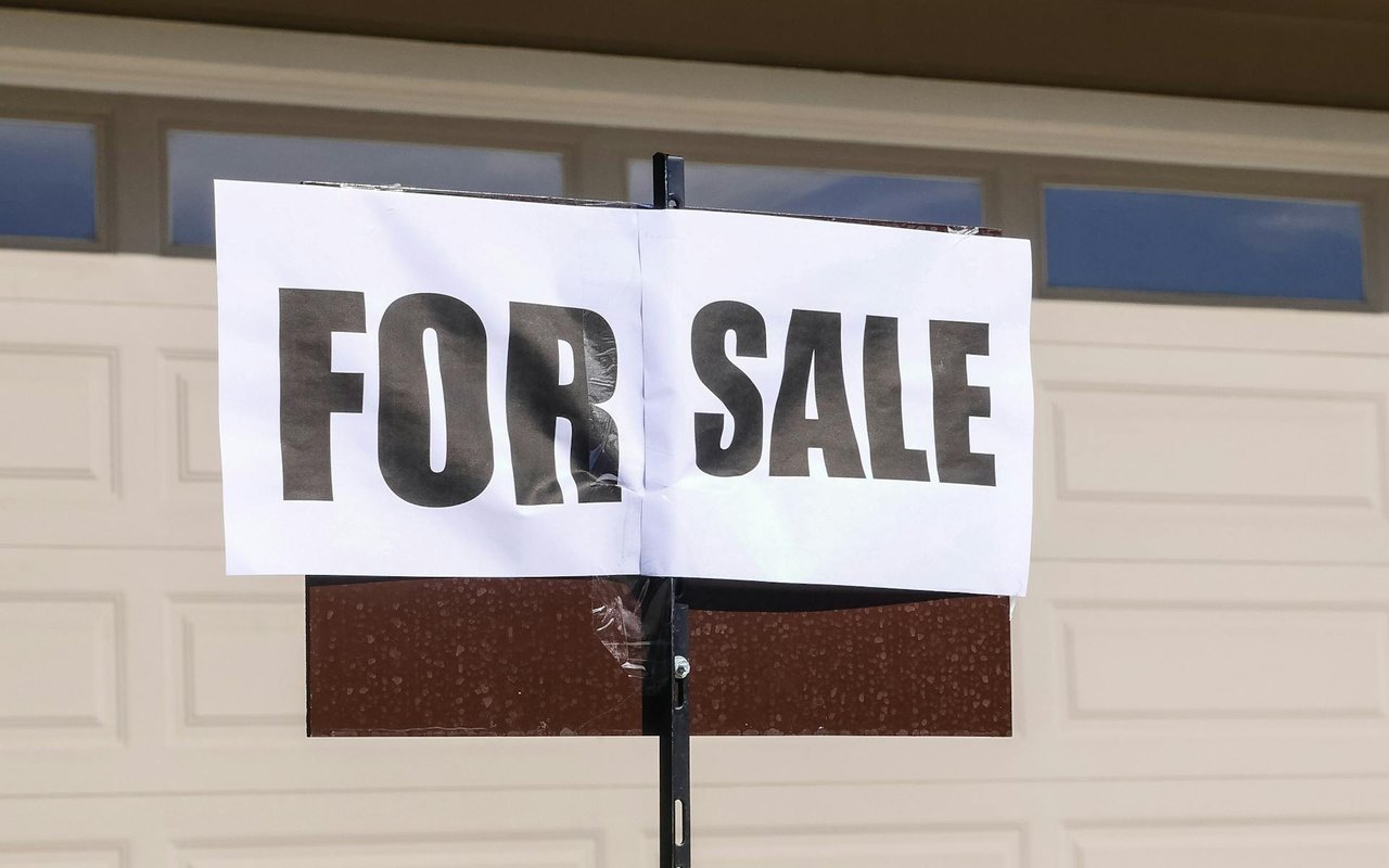 A paper FOR SALE sign attached to a post in front of a garage door.