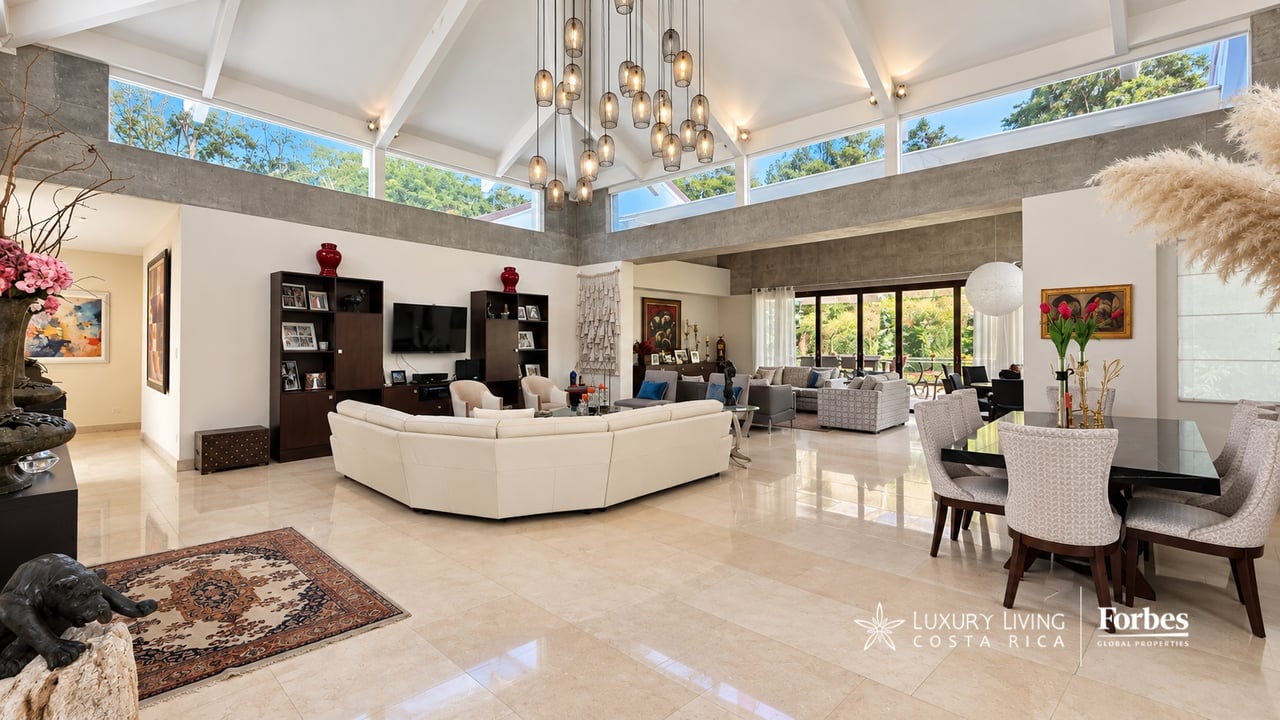 Open-plan living and dining room with a vaulted ceiling, pendant lights, and glass doors to greenery.