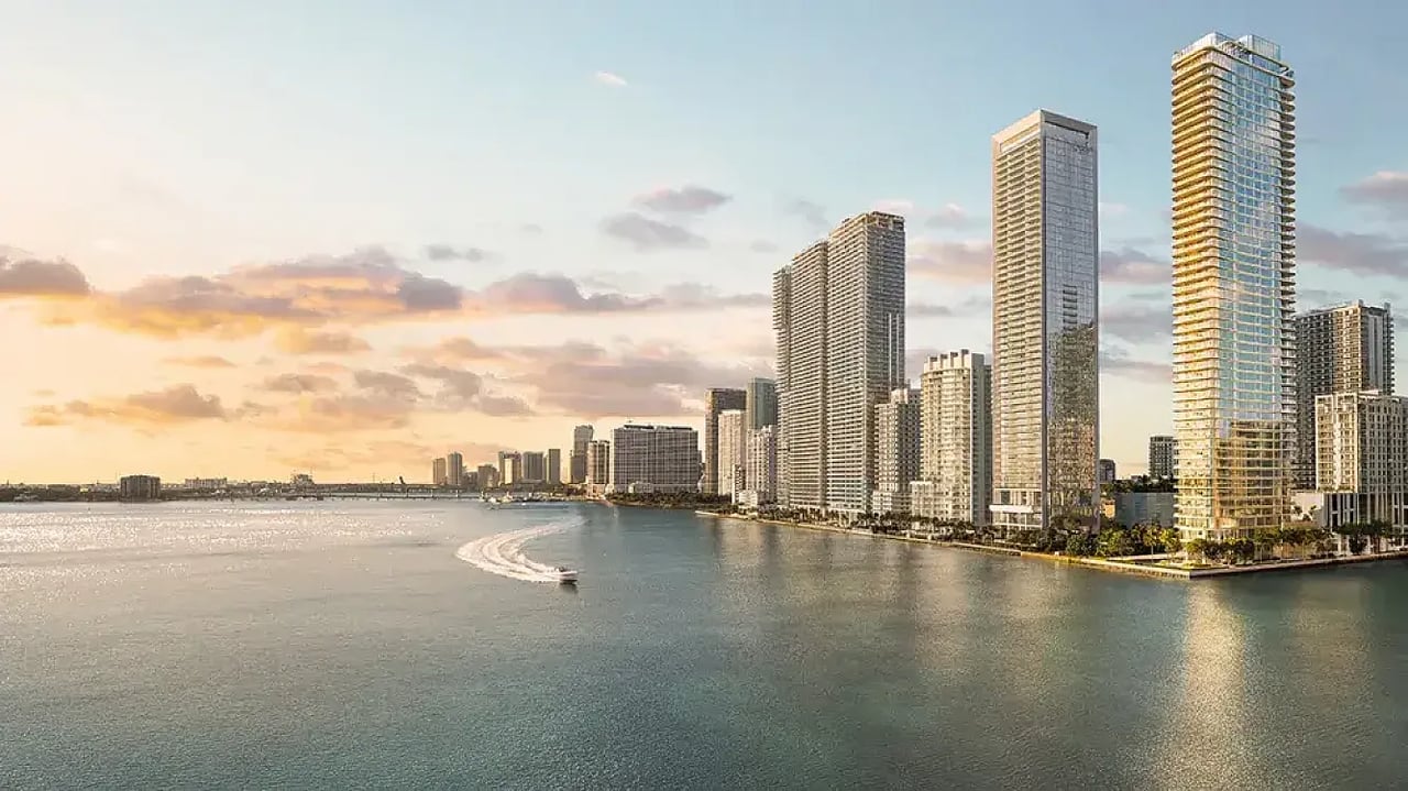 Residential towers line a waterfront bay as a boat leaves a curved wake.