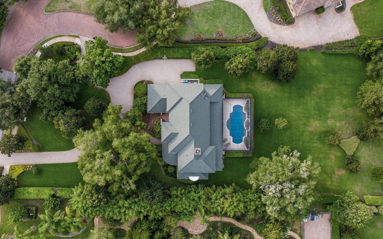 Aerial view of a landscaped home with a blue swimming pool beside it.