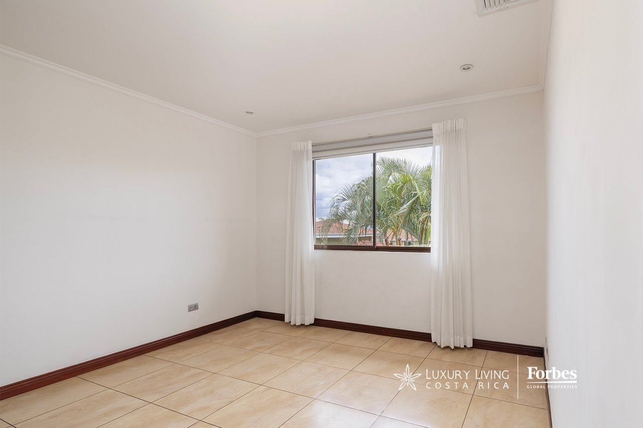 Empty bedroom with tiled floors, a curtained window, and palm trees outside.