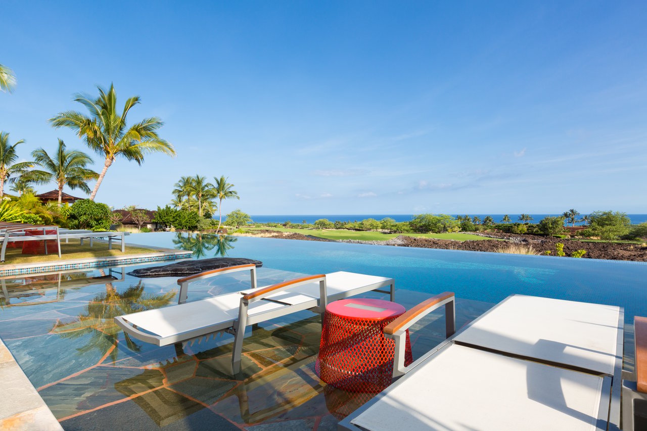 Infinity pool overlooking the ocean, with palm trees and white sun loungers.