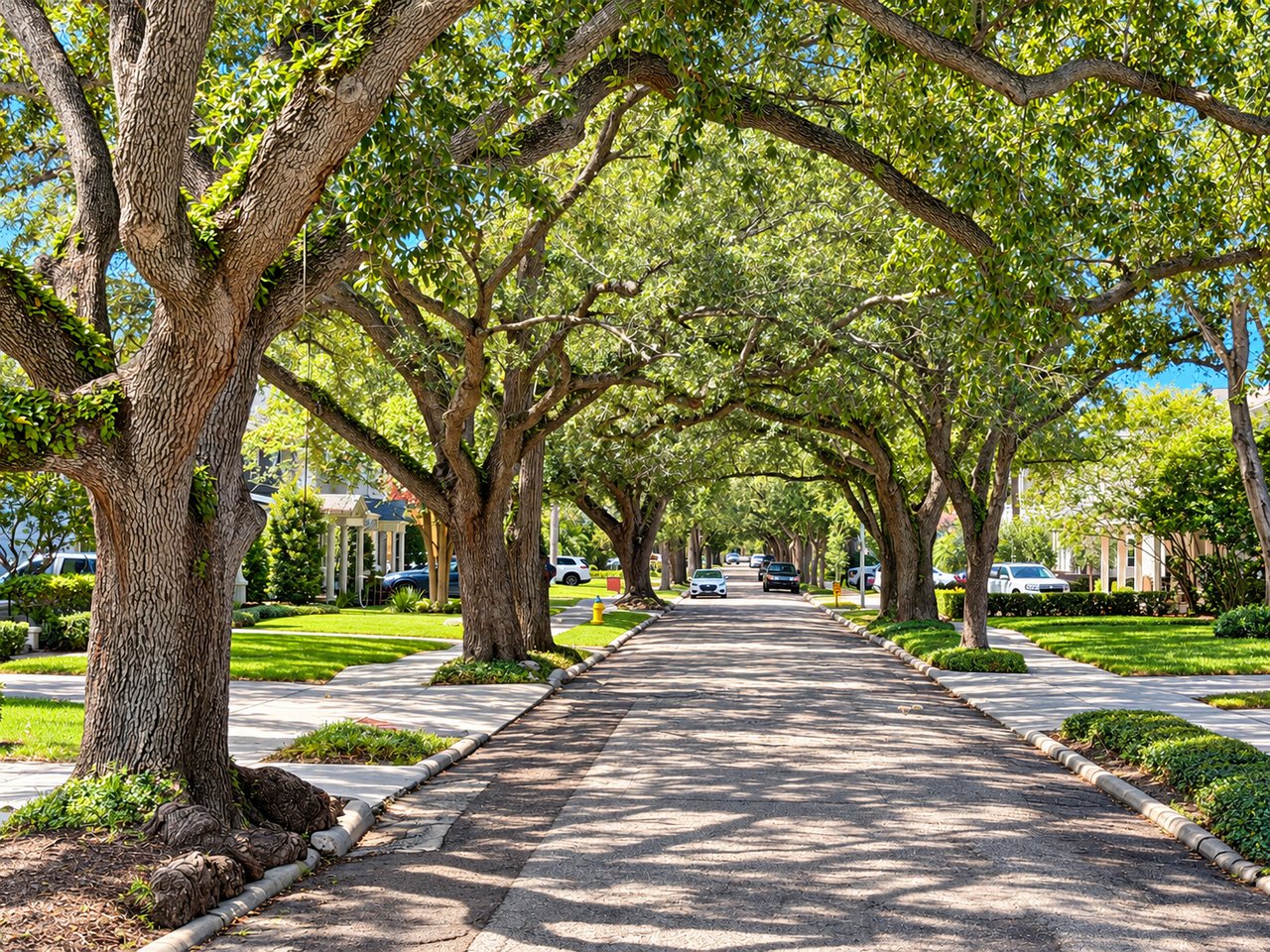 Tree-canopied residential street with homes, lawns, and parked cars