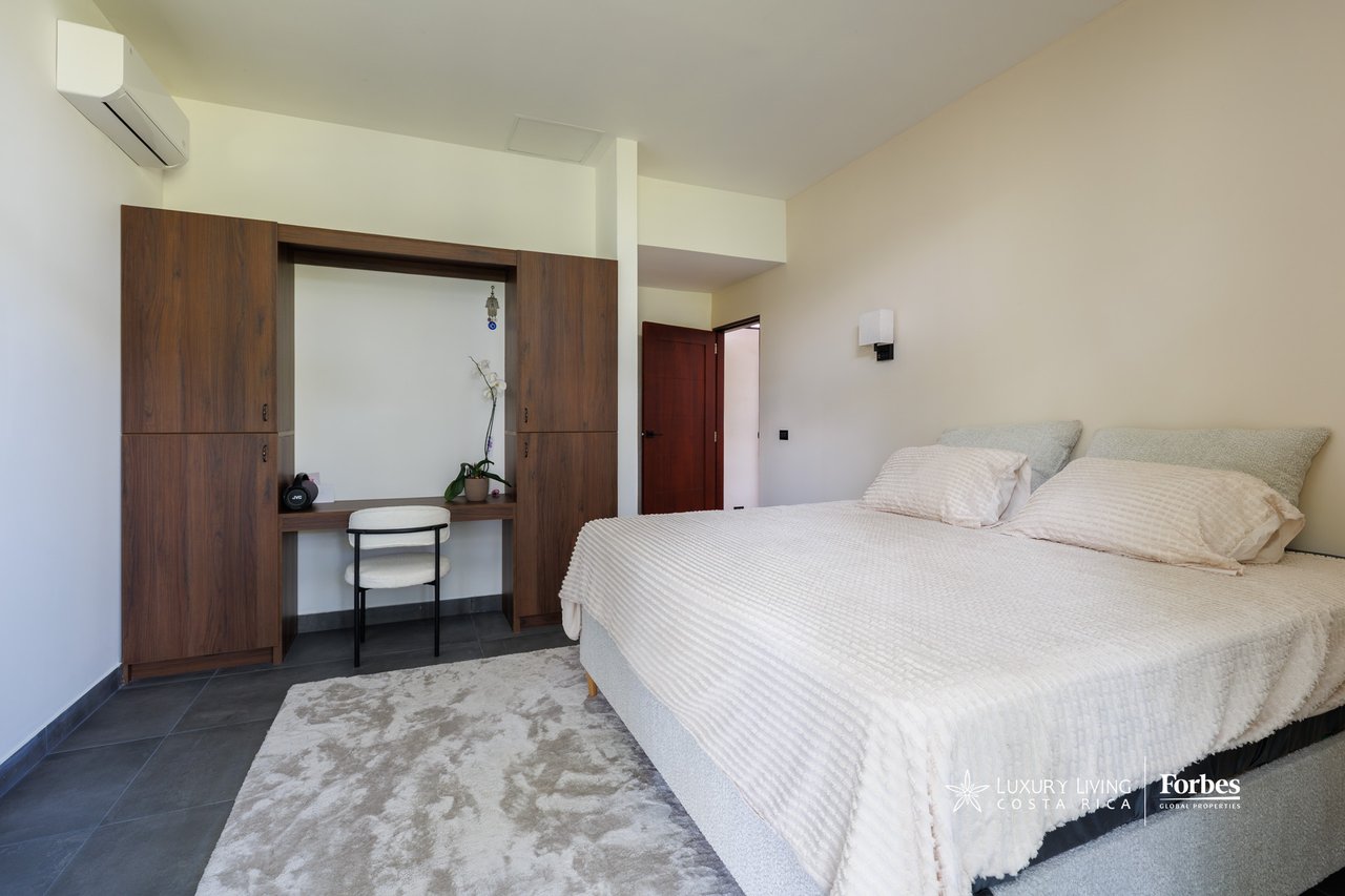 Bedroom with a white-covered bed and built-in dark wood desk and cabinets.