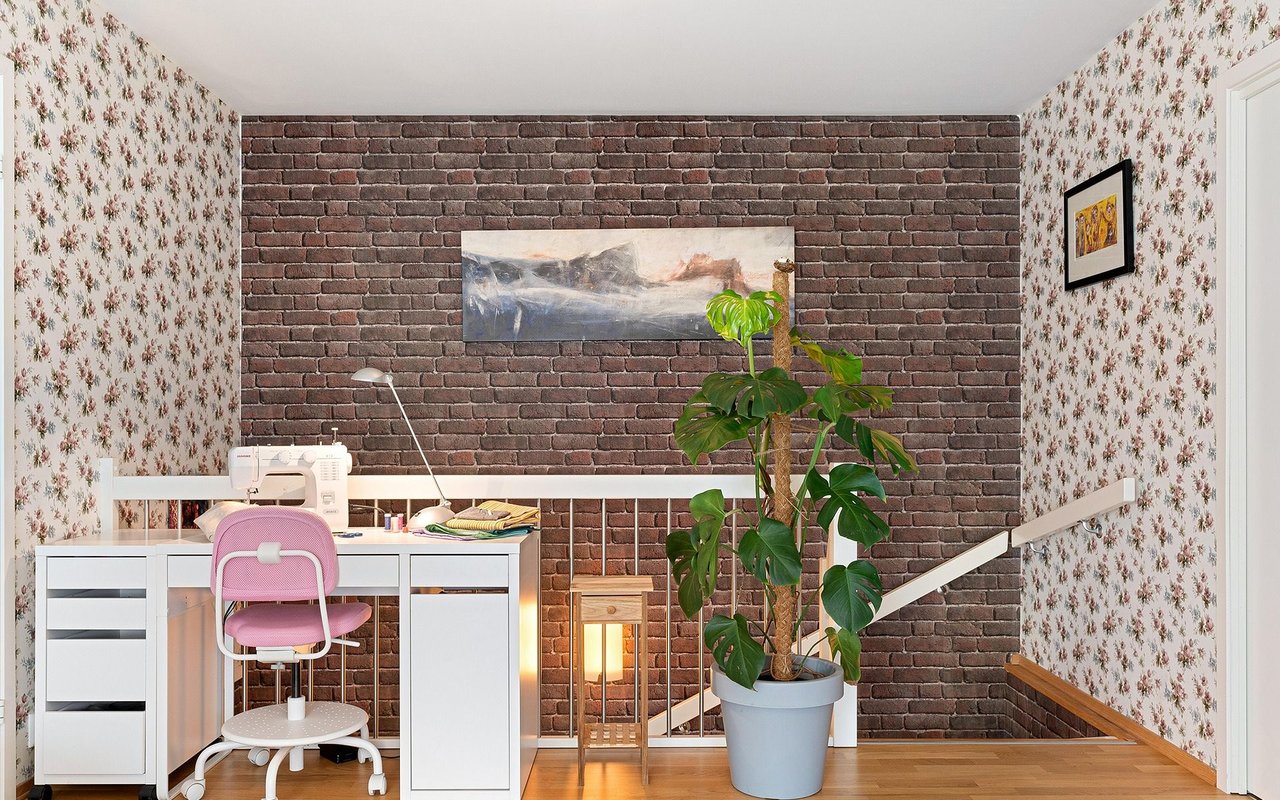 Home office with a sewing desk, exposed brick wall, floral wallpaper, and staircase.
