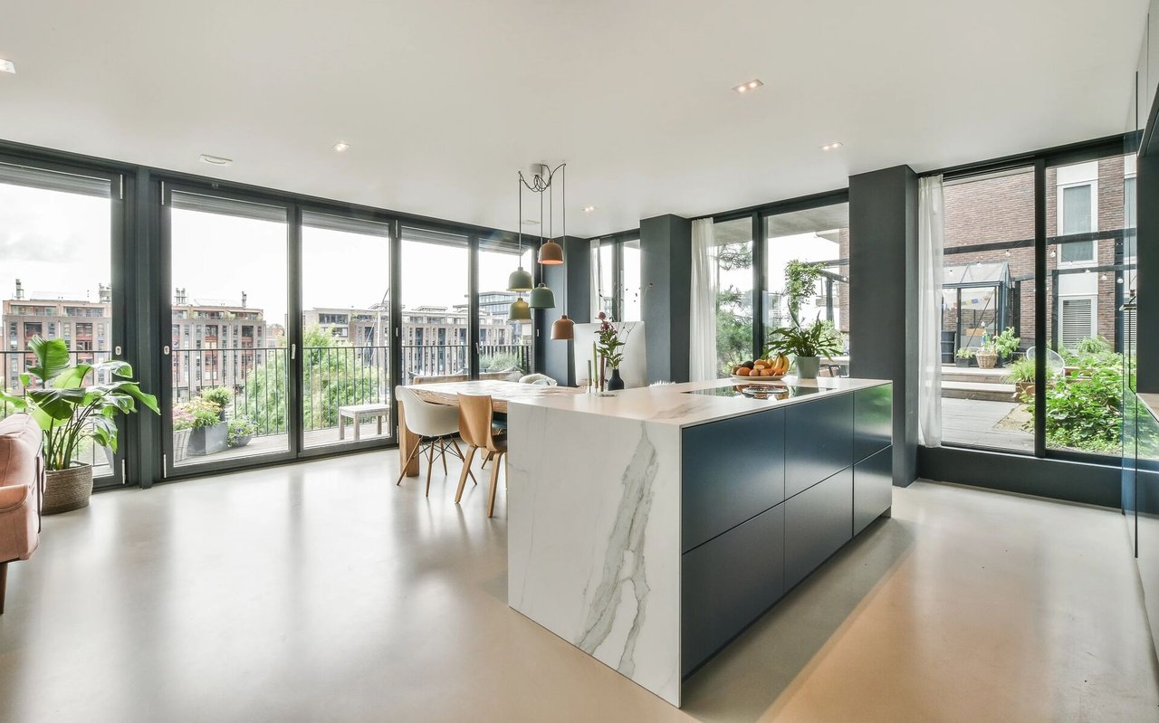 Modern kitchen with a marble island and floor-to-ceiling windows overlooking city buildings.